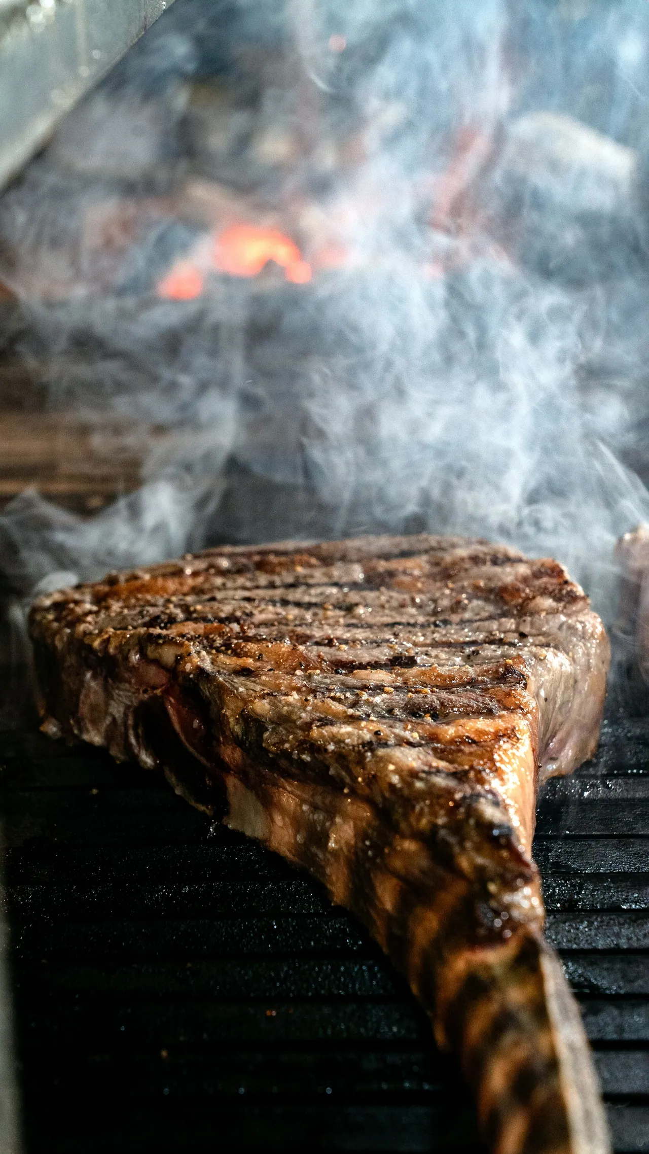 A steak grilling with smoke and flames on the flat-top